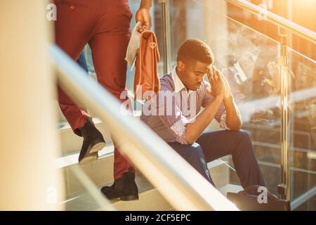 uomo d'affari nero stanco seduto sui gradini, la gente offuscava il movimento Foto Stock