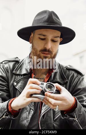 Giovane uomo bearded bello in cappello nero e giacca in pelle scattare foto in strada Foto Stock