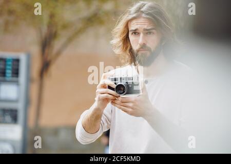 Giovane uomo bearded bello in vestiti casual scattando foto dentro via Foto Stock
