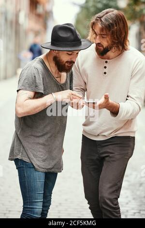 Bell'uomo in cappello nero in piedi con un amico in strada e puntare verso il telefono cellulare Foto Stock