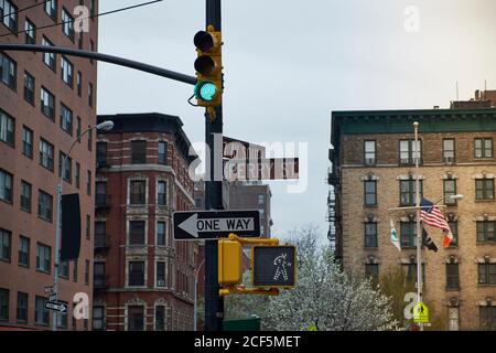 Basso angolo di segnaletica con vari cartelli stradali e verde Semaforo nel vecchio quartiere di New York City con edifici stagionato sullo sfondo Foto Stock