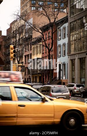 Taxi auto gialla che guida al bivio del centro storico Con tipici edifici in pietra in nuvoloso giorno di primavera a New Città di York Foto Stock