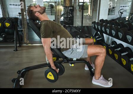 Uomo forte che si esercita con manubri in palestra Foto Stock