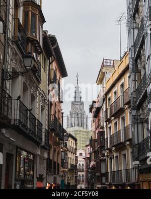 Dal basso della strada stretta della città di Toledo in Spagna con vecchi edifici residenziali e cattedrale sullo sfondo grigio cielo nuvoloso Foto Stock