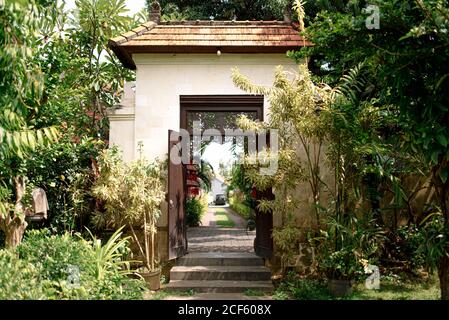 Passerella in pietra che conduce all'ingresso di cottage circondato da esotici Piante in giornata di sole a Bali Foto Stock