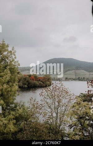 Splendido paesaggio tranquillo di lago circondato da verde foresta e. Montagne nebbie in un giorno di autunno nuvoloso in Scozia Foto Stock