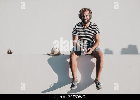 Giovane maschio seduto con smartphone e cuffie Foto Stock