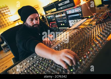 uomo musicista che lavora mentre suona in uno strumento di equalizzazione in uno studio Foto Stock