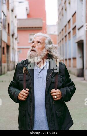 Turista maschile in giacca casual a piedi vicino a edifici shabby mentre esplorare la città durante le vacanze guardando via Foto Stock