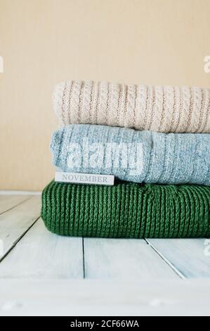 immagine verticale di una pila di pullover a maglia calda Colori pastello e l'iscrizione novembre su un legno chiaro tavolo in camera Foto Stock