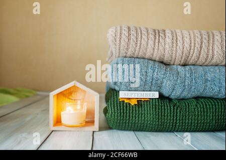 candela che brucia in casa di legno lampada e pila di maglia Pullover caldi in colori pastello e l'iscrizione Settembre e. foglia d'autunno su legno chiaro Foto Stock