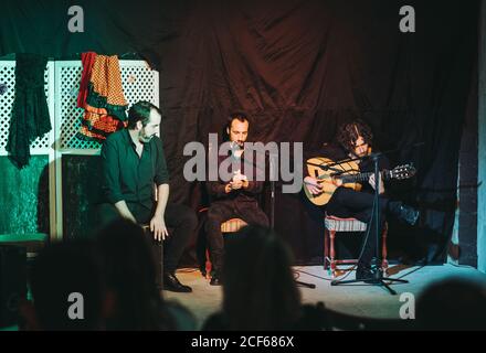 Band di musicisti ispanici maschili in nero indossati sedie di legno mentre suonano la chitarra acustica e cantano la canzone di flamenco nel microfono sull'a Foto Stock