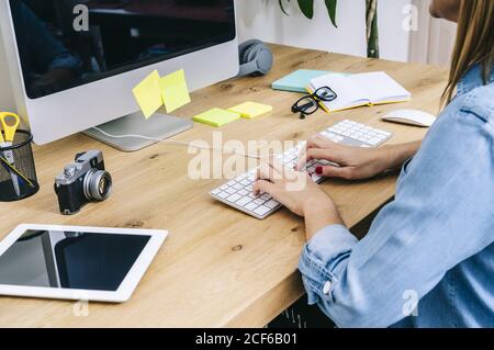 Crop donna caucasica irriconoscibile seduto su una scrivania di legno che lavora su un computer in un moderno ufficio domestico Foto Stock
