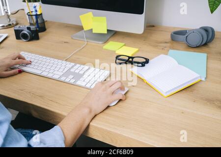 Crop donna caucasica irriconoscibile seduto su una scrivania di legno che lavora su un computer in un moderno ufficio domestico Foto Stock