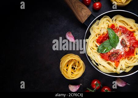 Dall'alto, deliziose tagliatelle servite in padella con pomodoro salsa e foglie di basilico fresco su fondo nero Foto Stock