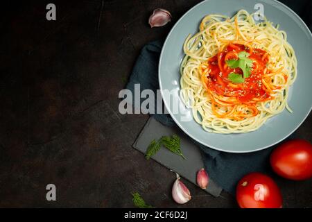 Vista dall'alto del piatto in ceramica blu con pasta e pomodoro salsa decorata con prezzemolo e basilico servito tra chiodi di garofano aglio e un paio di pomodori su sfondo scuro Foto Stock
