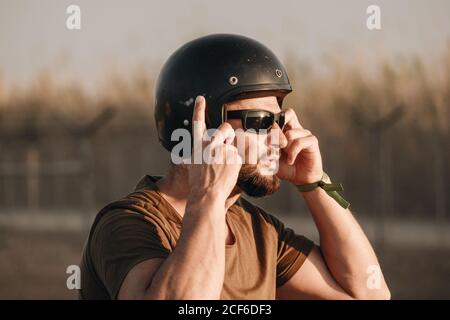 Vista laterale di un uomo brutale in occhiali da sole e casco su sfondo sfocato Foto Stock