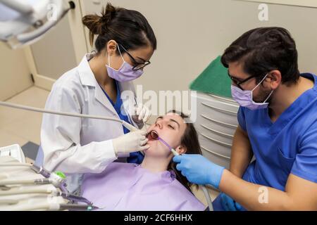 Dall'alto giovane dentista femminile in maschera e occhiali con assistente trattamento denti di Donna in clinica stomatologia Foto Stock