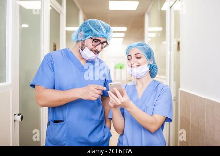 I colleghi chirurghi uomo e donna chiacchierano mentre camminavano verso la sala operatoria, gli mostra lo smartphone e sorridendo Foto Stock