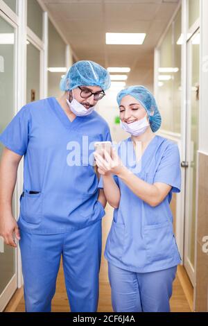 I colleghi chirurghi uomo e donna chiacchierano mentre camminavano verso la sala operatoria, gli mostra lo smartphone e sorridendo Foto Stock