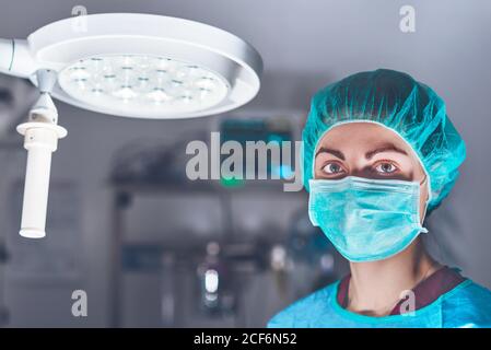 Donna adulta in maschera medica e cappello guardando la macchina fotografica prima di eseguire un intervento chirurgico in ospedale Foto Stock