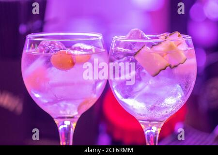 Closeup di bicchieri con fresco cocktail tonico alcolico con ghiaccio cubetti e frutta serviti su sfondo al neon sfocato durante la notte festa Foto Stock