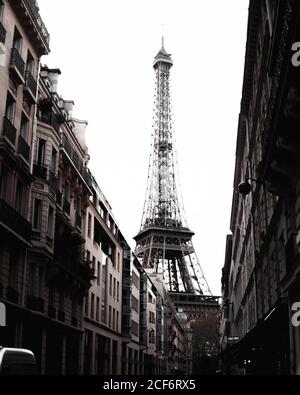 Esterno monocromatico dell'alta e splendida Torre Eiffel alla fine di strada stretta con vecchi e bei edifici monumentali sullo sfondo Cielo bianco luminoso a Parigi Foto Stock