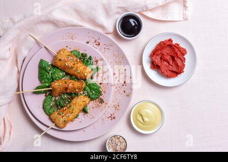 Spiedini di pollo in pastella fritti in panko fritto sul tavolo del ristorante con concentrato di pomodoro, salsa di soia, salsa di senape, spezie e spinaci orientali Foto Stock