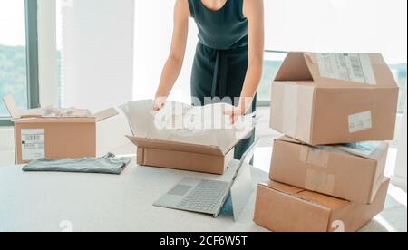 Vendere abbigliamento da casa. Piccola impresa imprenditore donna che impacchettano vestiti di vestito in scatola spedente per la spedizione dal deposito in linea Foto Stock