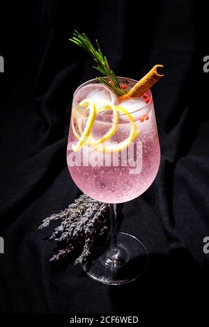 Cocktail tonico gin con acqua tonica rosa, pepe rosa, rosmarino, menta, cannella, limone e arancio su sfondo scuro Foto Stock