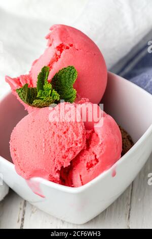 Dall'alto viene servito un delizioso gelato rosa con foglie di menta su sfondo di legno e tessuto Foto Stock