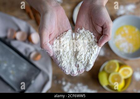 Vista dall'alto della donna irriconoscibile e tagliata che mostra le mani piene di farina vicino al recipiente nero mentre prepari la pasta a casa Foto Stock