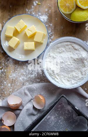 Vista dall'alto degli ingredienti per la ricetta della torta, inclusa la ciotola con farina e uovo posti su tavola di legno spolverato Foto Stock