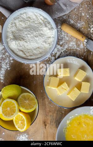 Vista dall'alto degli ingredienti per la ricetta della torta, inclusa la ciotola con farina e uovo posti su tavola di legno spolverato Foto Stock