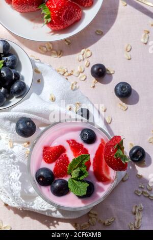 Yogurt fatto in casa con fragole, mirtilli e cereali dall'alto con tovaglie rosa e Sunlight.Healthy food concept.Vegan food Foto Stock