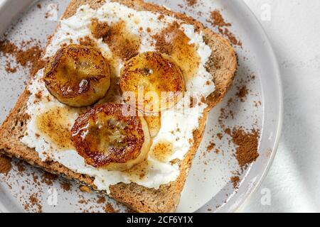 Pane tostato fatto in casa con formaggio spalmabile, banana fritta, miele e cannella.concetto alimentare vegetariano. Foto Stock