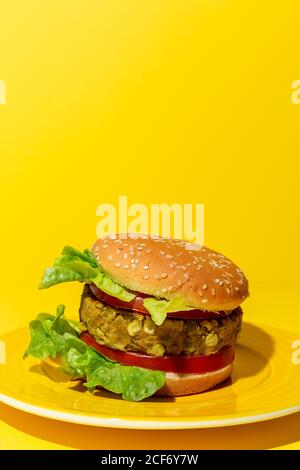 Hamburger di lenticchie verdi vegane fatto in casa con pomodoro, lattuga e patatine fritte su uno sfondo giallo colorato Foto Stock