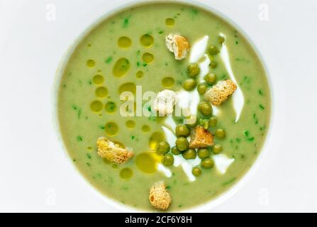 Da sopra purè di zuppa cremosa di verdure con piselli verdi e. piccoli cracker su sfondo bianco Foto Stock