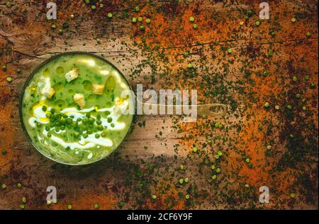 Dall'alto purè di zuppa cremosa di verdure con piccoli cracker e. piselli verdi su padella su sfondo di legno Foto Stock