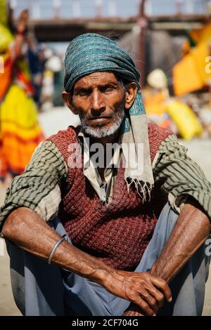 Allahabad, India - FEBBRAIO, 2018: Primo piano ritratto di anziano indiano che indossa abiti tradizionali seduti sul pavimento contro sfondo sfocato Foto Stock