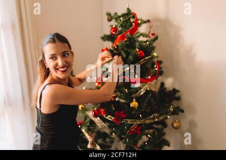 Felice giovane donna decorazione albero di natale con palla a casa Foto Stock