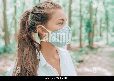 Maschera facciale in tessuto di cotone traspirante per la pelle. Donna asiatica che indossa la bocca del virus corona che copre camminando all'aperto nei boschi Foto Stock
