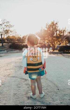 Vista posteriore della bambina carina con zaino in piedi terreno sabbioso nel parco Foto Stock