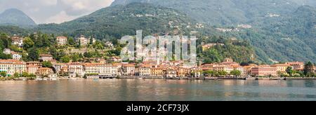 Panorama della città di Menaggio sul Lago di Como in Italia. Architettura luminosa con edifici colorati. Città Embankment con i turisti. Vista dall'acqua. Foto Stock