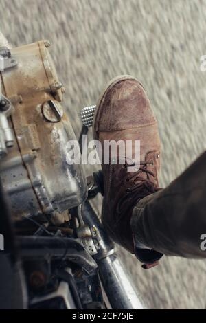 Gamba di anonimo uomo che si fa salire sul pedale della moto durante guidare su strada asfaltata Foto Stock
