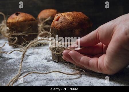 Crop persona che organizza spago su dolci di Natale fatti in casa appena sfornati posto su tavola in polvere con farina bianca Foto Stock