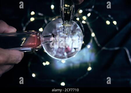 Dall'alto del barista anonimo raccolto che versa varie bevande da bottiglie in shaker con cubetti di ghiaccio mentre si prepara un cocktail alcolico nel bar Foto Stock