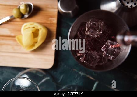 Da sopra il processo di versamento della bevanda alcolica rossa dal flacone in shaker con cubetti di ghiaccio durante la preparazione del cocktail al bancone Foto Stock