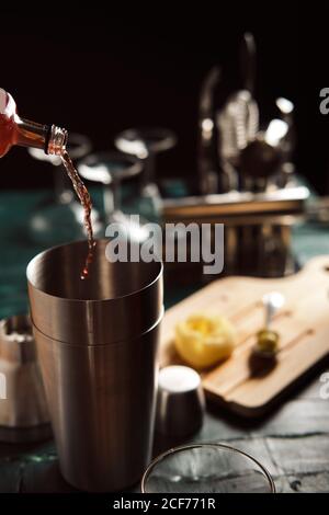 Da sopra il processo di versamento della bevanda alcolica rossa dal flacone in shaker con cubetti di ghiaccio durante la preparazione del cocktail al bancone Foto Stock