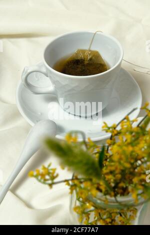 Da sopra tazza bianca con il tè messo sul letto con bouquet di fiori gialli per una deliziosa colazione a letto Foto Stock